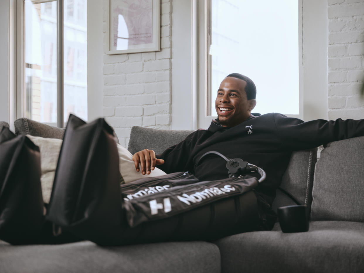 Alex Toussaint sitting on a couch smiling wearing the Normatec.