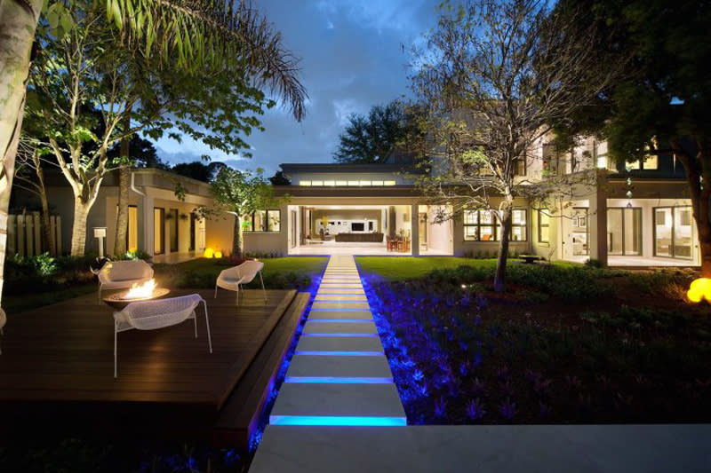 <p>Fiery heat and cobalt blue landscape lighting add up to a dramatically pretty back yard in this Washington home. Copy this look by dressing up your deck with a firepit and some modern seating.</p>