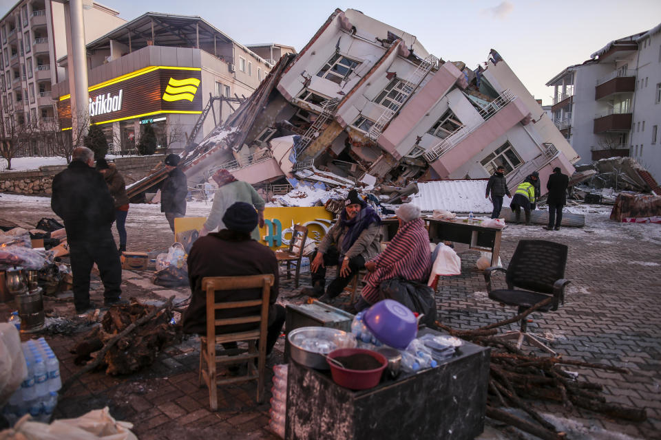 People sit and stand around a collapsed building in Golbasi, Adiyaman province, southern Turkey, February 8, 2023, several days after devastating earthquakes hit the region. / Credit: Emrah Gurel/AP