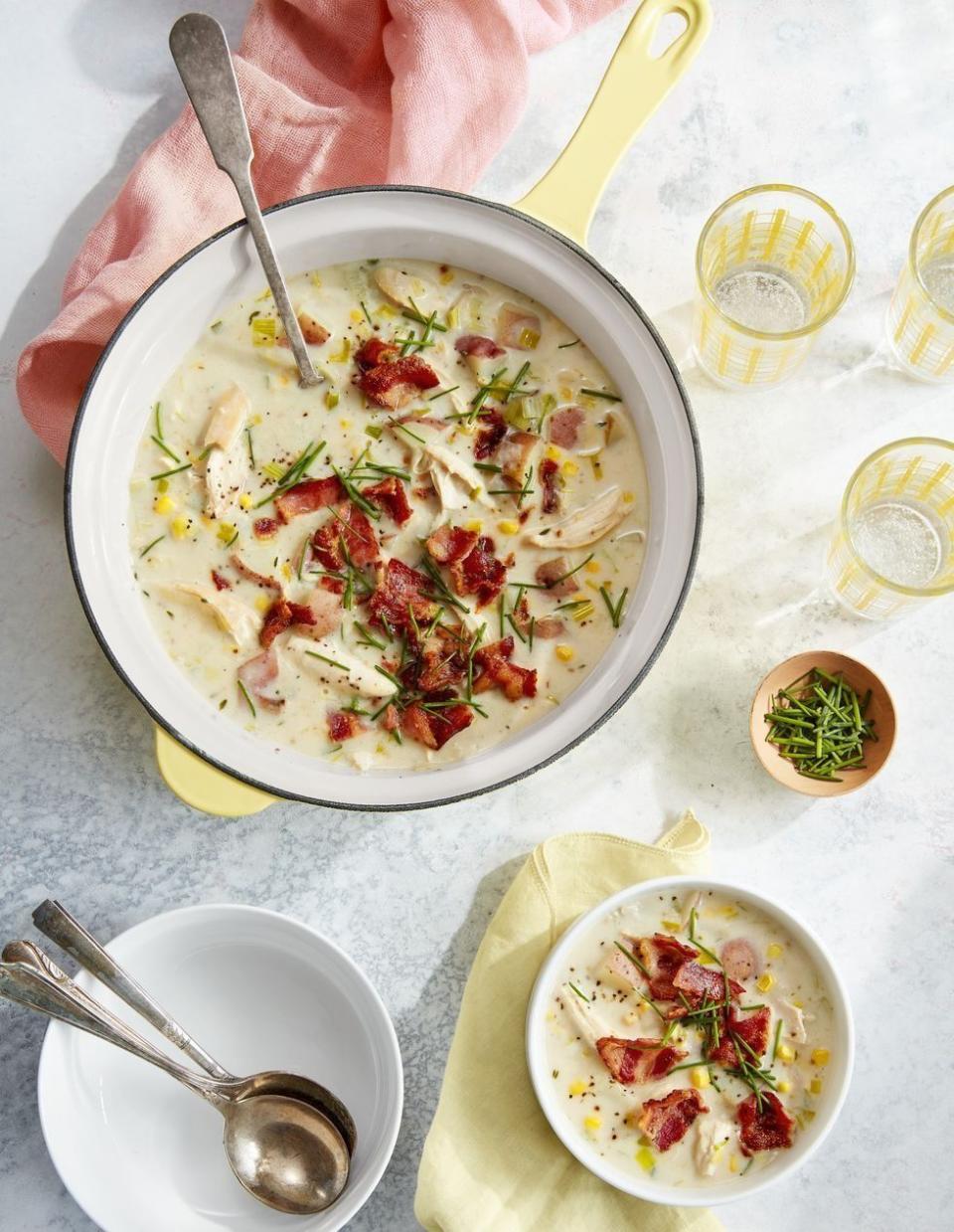 creamy chicken soup with potatoes and bacon in a saucepan and some in a bowl next to it and a bowl of spoons