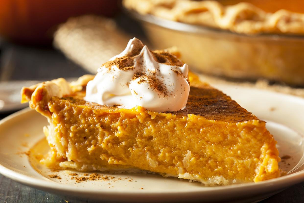 One piece of crustless pumpkin pie on a tan plate with a blurred background of pie and a napkin