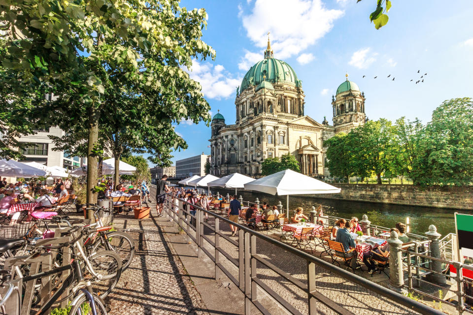 Crowds dining by riverside near historic cathedral with clear skies