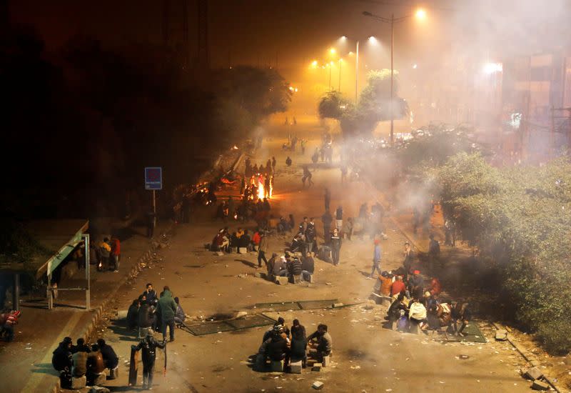 Local residents sit next to bonfires as they block a road during a protest against a new citizenship law, in New Delhi