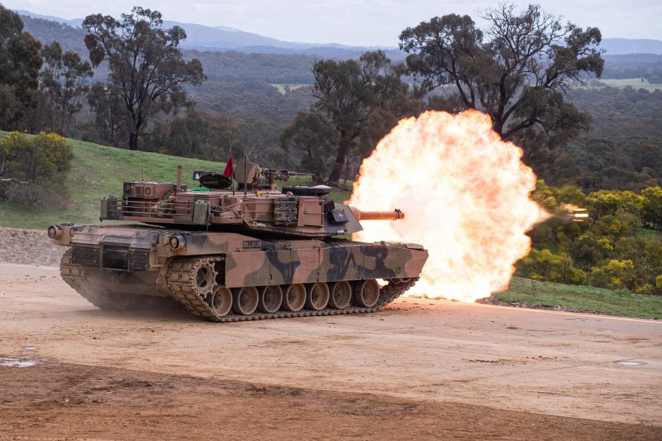 An Abrams tank on a hill firing, causing an explosion.