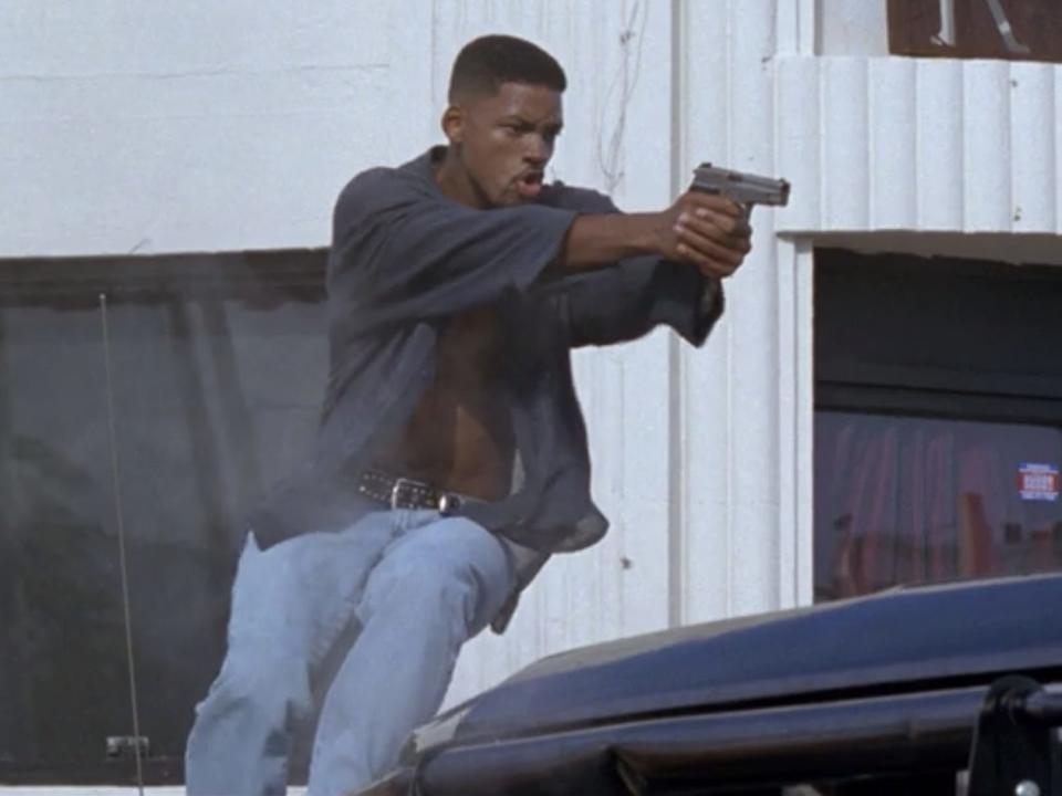 Will Smith wearing an unbuttoned shirt and running with a gun in 