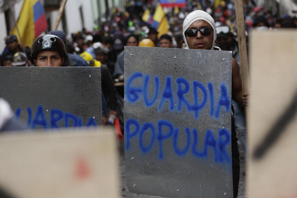 Anti-government demonstrators march with makeshift shields sprayed painted with the Spanish words for, "The People's Guard", during a nationwide strike against President Lenin Moreno and his economic policies, in Quito, Ecuador, Wednesday, Oct. 9, 2019. Ecuador's military has warned people who plan to participate in a national strike over fuel price hikes to avoid acts of violence. The military says it will enforce the law during the planned strike Wednesday, following days of unrest that led Moreno to move government operations from Quito to the port of Guayaquil. (AP Photo/Carlos Noriega)