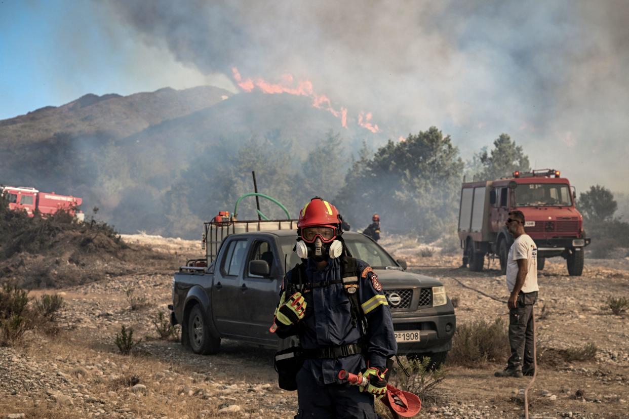 A firefighter looks on as wildfires burn a hillside near the village of Vati, just north of the coastal town of Gennadi, in the southern part of the Greek island of Rhodes, July 25, 2023. / Credit: SPYROS BAKALIS/AFP/Getty