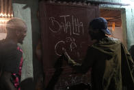 Rap artist Roque writes "Gas Battle" on the door of a bar to announce an upcoming rap competition in the City of God favela in Rio de Janeiro, Brazil, late Wednesday, Nov. 10, 2021. Rap artists in the favela are starting to compete again since the COVID-19 pandemic curtailed public gatherings, presenting local residents with a show in a sign of a return to normalcy for music lovers. (AP Photo/Silvia Izquierdo)