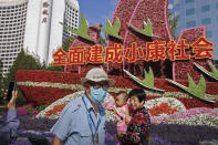 A man wearing a face mask to help curb the spread of the coronavirus walks by a woman with a child posing for a souvenir photo near a floral decoration baring the words "Fully built a well-off society" for celebrating the up-coming National Day in Beijing, Wednesday, Sept. 30, 2020. Even though the spread of COVID-19 has been all but eradicated in China, the pandemic is still surging across the globe with ever rising death toll. (AP Photo/Andy Wong)