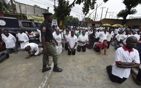 A policeman walks next to people kneeling as they pray for victims of violent attacks across Nigeria at Ikeja St Leo Catholic Church in Lagos - Credit:  PIUS UTOMI EKPEI/AFP