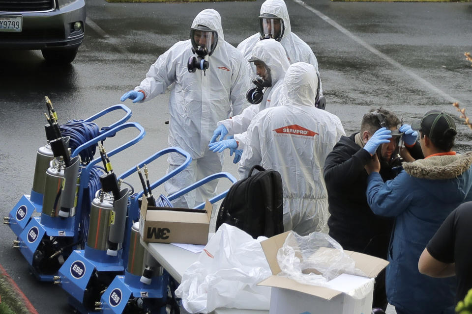 Workers from a Servpro disaster recovery team wearing protective suits and respirators more toward equipment as they line up before entering the Life Care Center in Kirkland, Wash. to begin cleaning and disinfecting the facility, Wednesday, March 11, 2020, near Seattle. The nursing home is at the center of the outbreak of the COVID-19 coronavirus in Washington state. (AP Photo/Ted S. Warren)