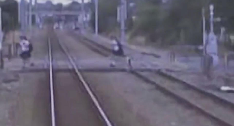 Two New Zealand school kids run over a crossing despite a train coming towards them.