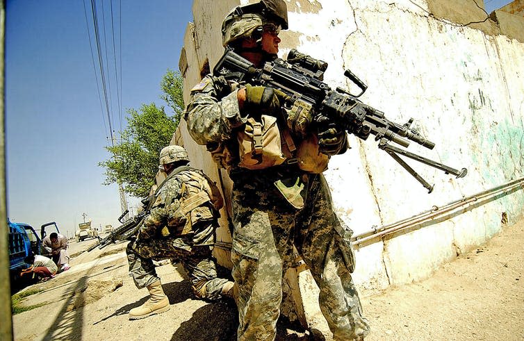 US army soldier stands guard at damanged street corner.