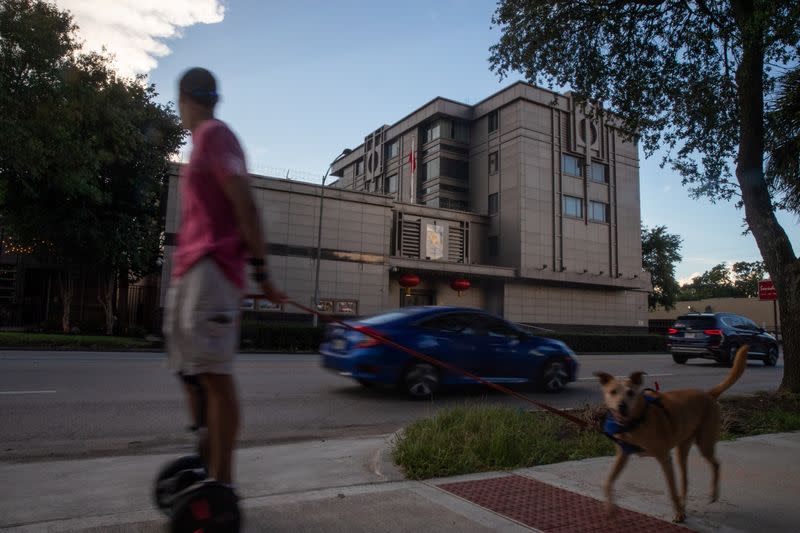 A man on a hoverboard walks his dog past the China Consulate General in Houston, Texas
