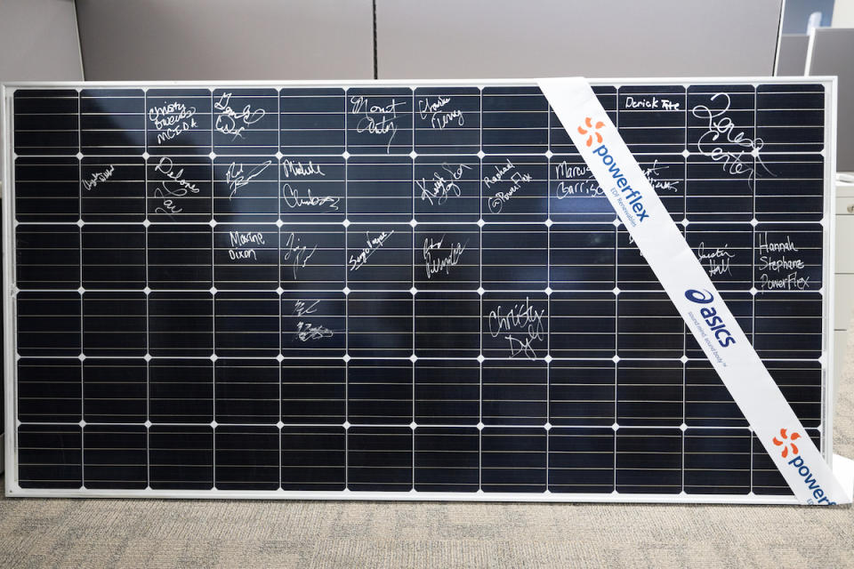 A solar panel with signatures and a co-branded PowerFlex and Asics ribbon draped across the corner.