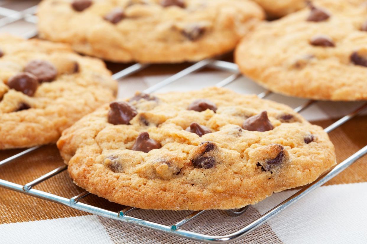 Closeup of four chocolate chip cookies on a metal wire baking sheet on a brown and white checkered tablecloth