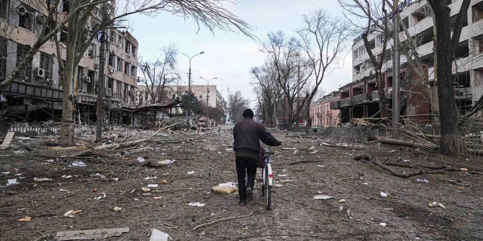 A man walks his bicycle down a damaged street.