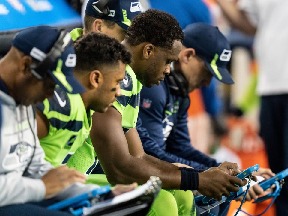 Geno Smith looks at a tablet on the sidelines during a game against the Los Angeles Rams.