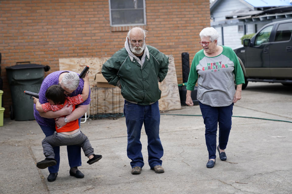 Janice Morgan, a church volunteer, hugs Conner Bourque as she arrives with Brenda Lee to bring him Christmas presents, in the aftermath of Hurricane Laura and Hurricane Delta, in Lake Charles, La., Friday, Dec. 4, 2020. Center is James Baker, who is living in a camper while his daughter lives in a tent outside of his heavily damaged home. (AP Photo/Gerald Herbert)