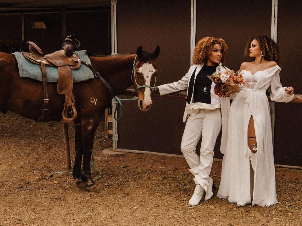 Two brides pose next to a horse.