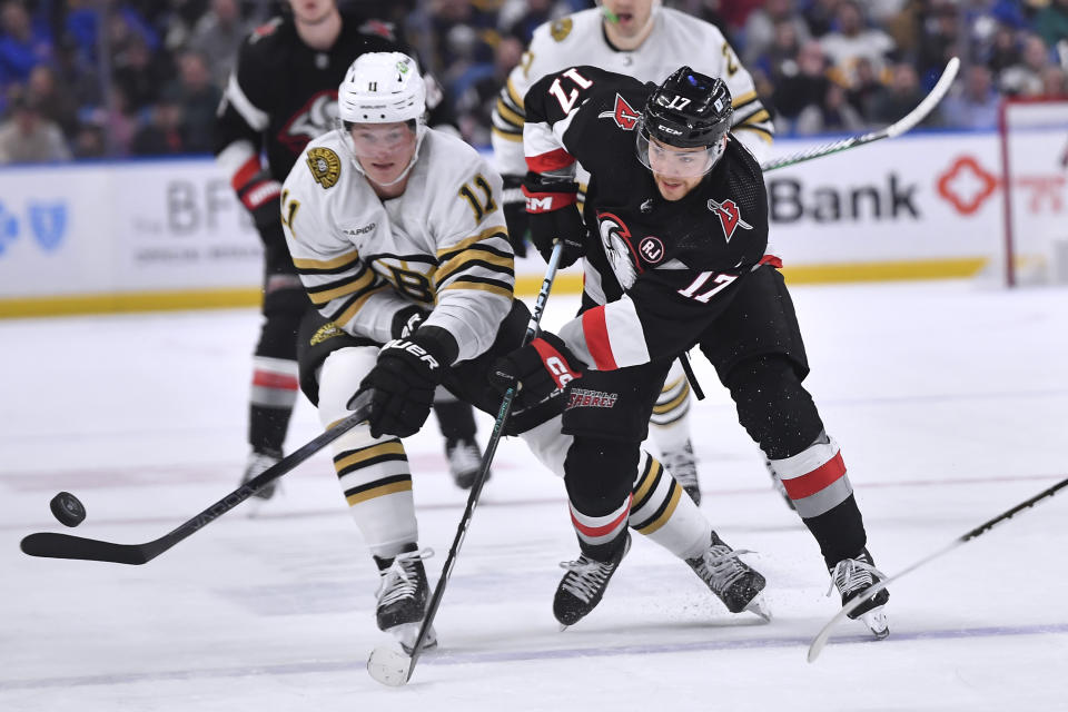 Boston Bruins center Trent Frederic, left, tips the puck away from Buffalo Sabres center Tyson Jost during the second period of an NHL hockey game in Buffalo, N.Y., Wednesday, Dec. 27, 2023. (AP Photo/Adrian Kraus)