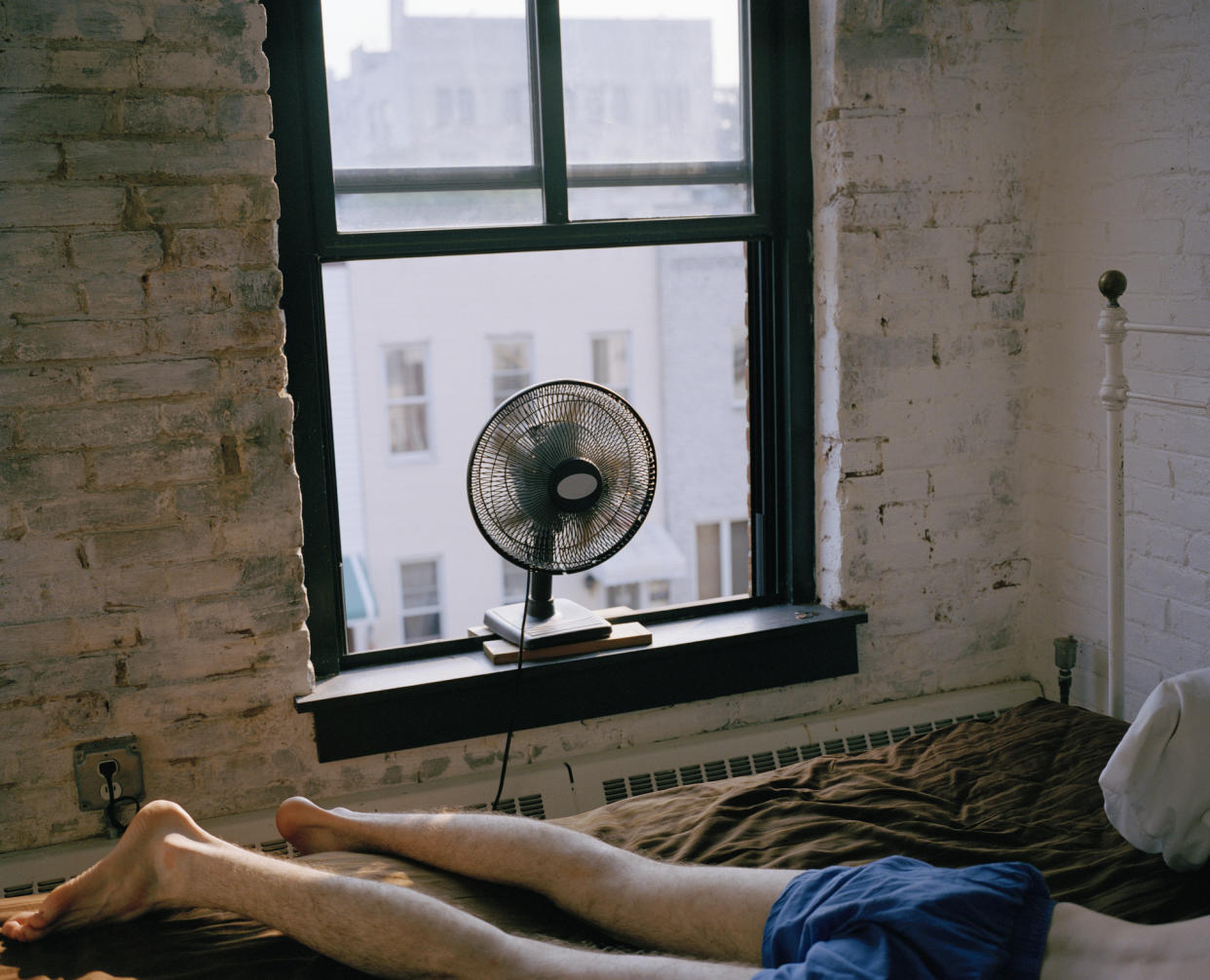 A man lying on a bed with a fan blowing