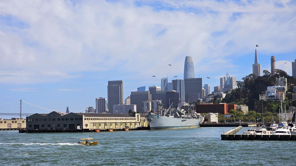 San Francisco city skyline with skyscrapers, viewed from the water, featuring boats and a large docked ship in the foreground