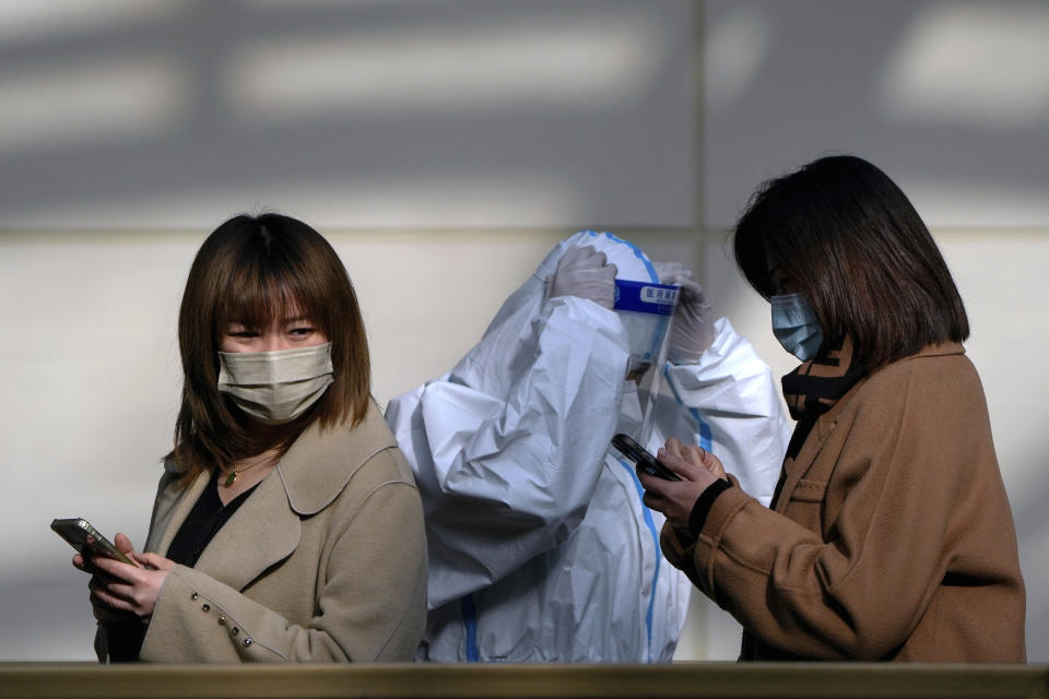 A worker in protective suit adjusts his face shield as women wearing face masks line up for their routine COVID-19 tests in Beijing, Monday, Dec. 5, 2022. China is easing some of the world's most stringent anti-virus controls and authorities say new variants are weaker. But they have yet to say when they might end a "zero-COVID" strategy that confines millions of people to their homes and set off protests and demands for President Xi Jinping to resign. (AP Photo/Andy Wong)