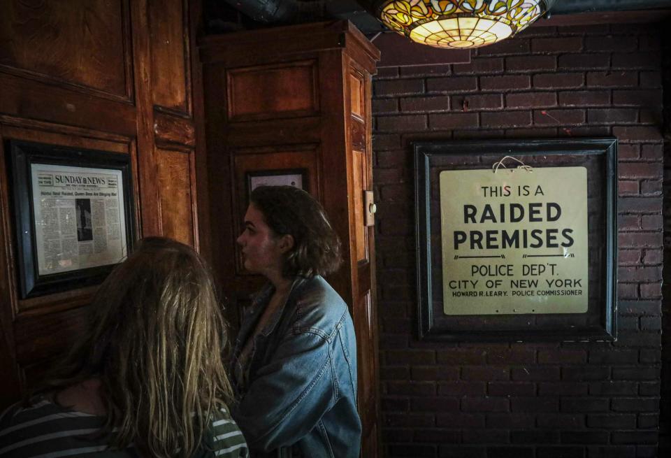 In this Friday June 14, 2019, photo, Stonewall Inn visitors read news clipping headlining the 1969 riots that followed a police raid of the bar in New York. Some of the coverage of rioting was itself a source of the fury that led Stonewall to become a synonym for the fight for gay rights.(AP Photo/Bebeto Matthews)