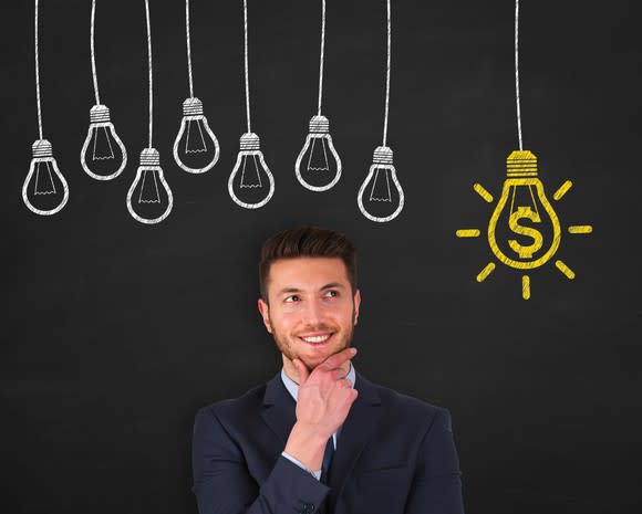 Man with hand on chin in front of chalkboard drawing of light bulbs with one light bulb with dollar symbol on it