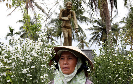 A woman arranges flower in front of a statue in a museum during the 50th anniversary of the My Lai massacre in My Lai village, Vietnam March 15, 2018. REUTERS/Kham