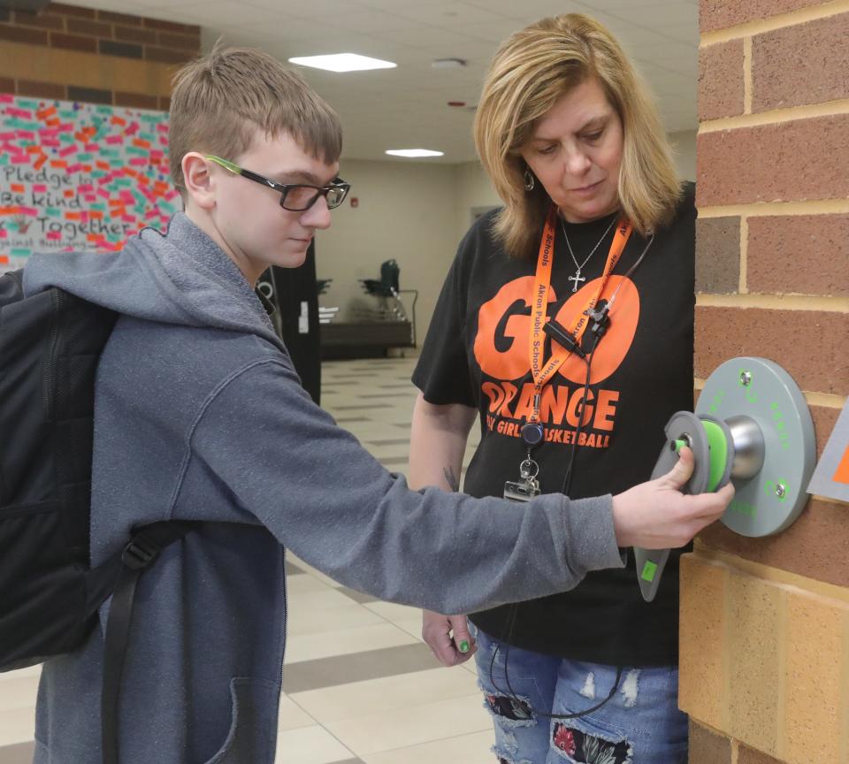 Ellet CLC freshman Keith Carlson unlocks his cellphone from a Yondr pouch at the end of the school day supervised by safety team member Luan Haas on Wednesday, March 8, 2023, in Akron.