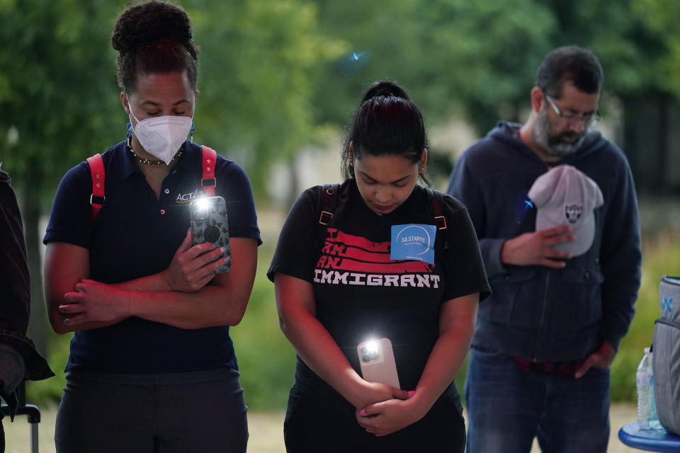 Naiyolis Paloma, center, prays with others during a community vigil for the dozens of people found dead Monday in a semitrailer containing suspected migrants as well as those who received heat related injuries, Tuesday, June 28, 2022, in San Antonio. Due to a flame ban, the group used artificial candles and cell phones. (AP Photo/Eric Gay)