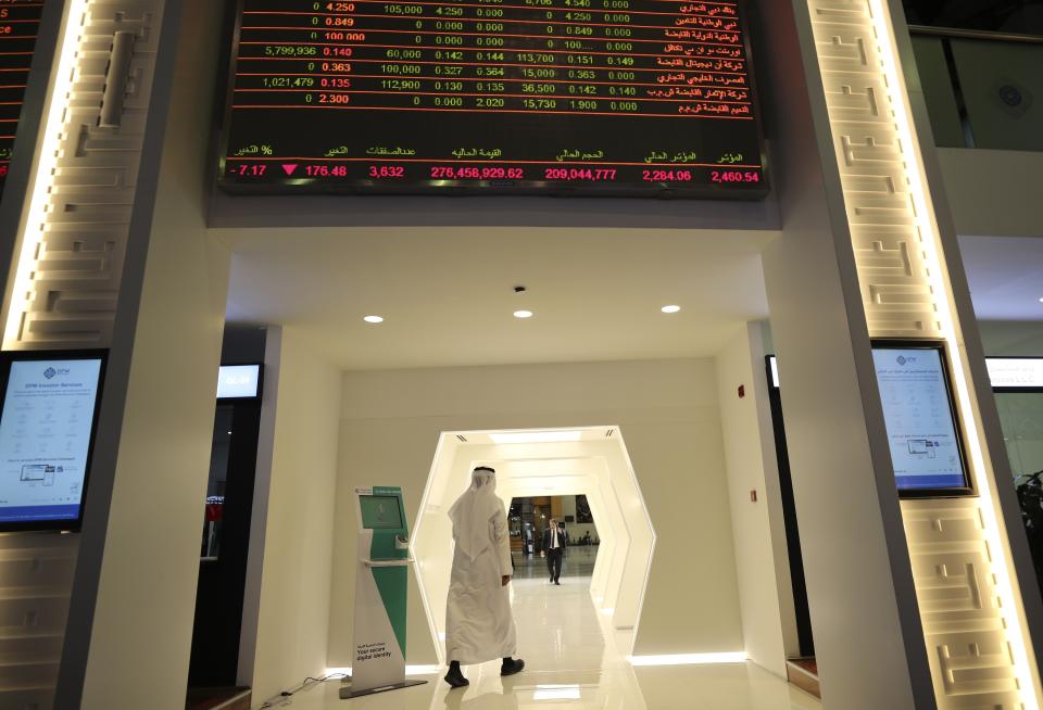 An Emirati trader passes under the stocks display screen at the Dubai Financial Market in Dubai, United Arab Emirates, Sunday, March 8, 2020. Stocks markets in the Mideast suffered sharp drops in early trading Sunday over fears about the new coronavirus and demand in crude oil falling amid a failure by OPEC and allied nations to cut production. (AP Photo/Kamran Jebreili)