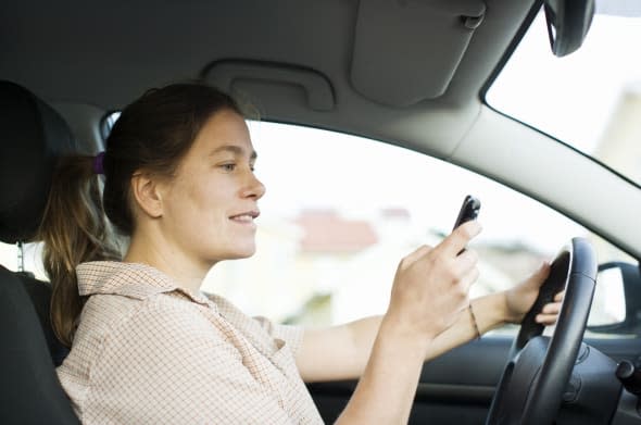 Mid adult woman dialing on mobile phone while driving