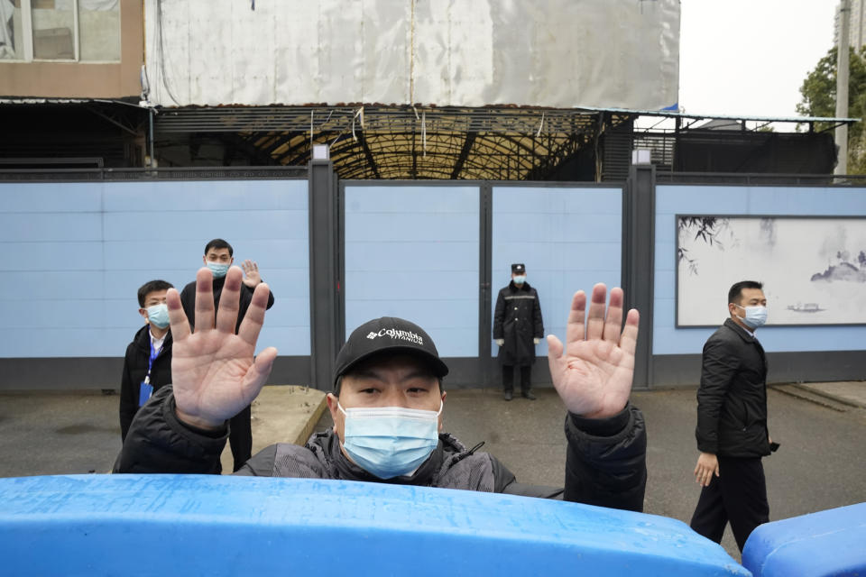 FILE - In this Jan. 31, 2021, file photo, a security guard waves for journalists to clear the road after a convoy carrying the World Health Organization team entered the Huanan Seafood Market on the third day of a field visit in Wuhan in central China's Hubei province. A member of the expert team investigating the origins of the coronavirus in Wuhan says the Chinese side granted full access to all sites and personnel they requested to visit and meet with. (AP Photo/Ng Han Guan, File)