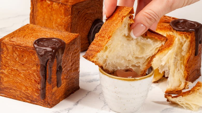 Dipping slice of croissant cube in chocolate