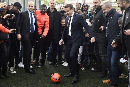 Emmanuel Macron (C), head of the political movement En Marche !, or Onwards !, and candidate for the 2017 presidential election, kicks a soccer ball during a campaign visit in Sarcelles, near Paris, April 27, 2017. REUTERS/Martin Bureau/Pool