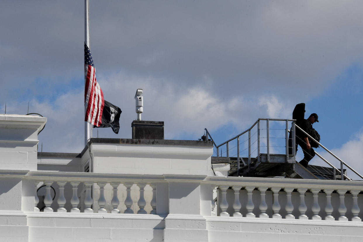 A Secret service sniper walks past the flag that was lowered atop the White House following the death of former Secretary of State Colin Powell on Monday. (Photo by Olivier Douliery/AFP via Getty Images)