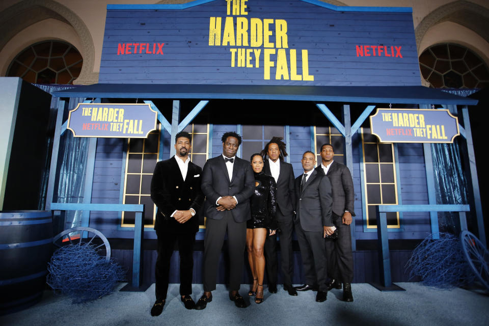 "The Harder They Fall" cast and production members pose in front of a pop-up saloon at an event for the film