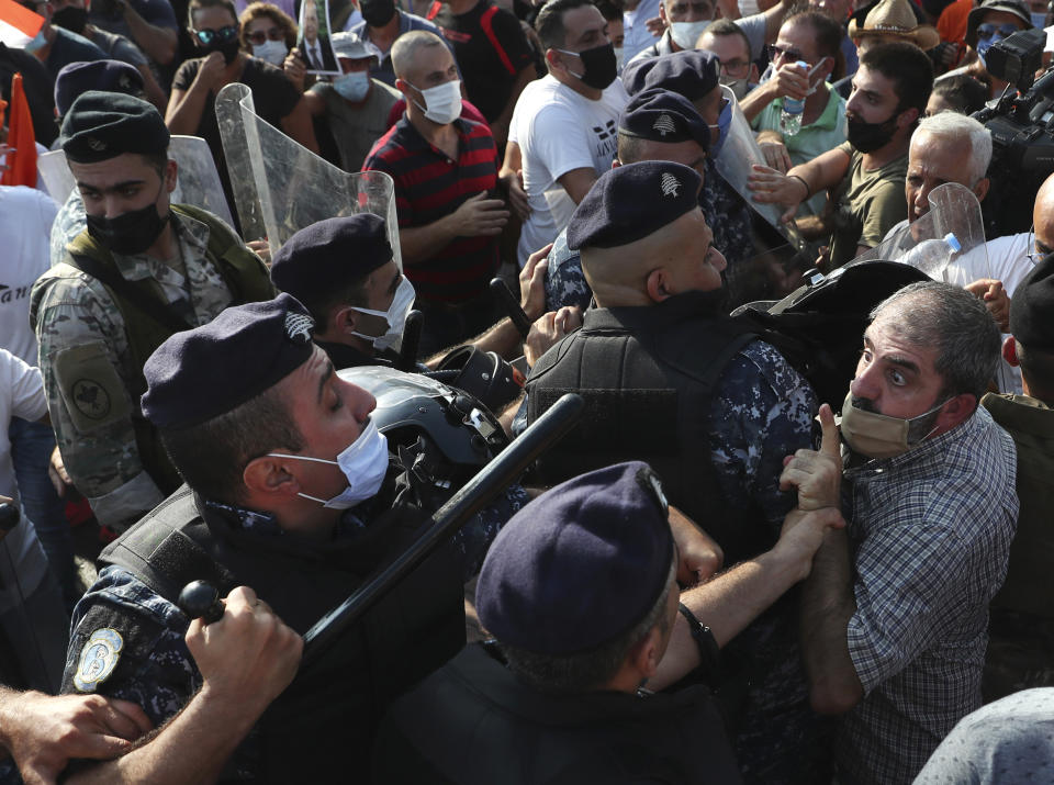 A supporter of Lebanese President Michel Aoun argues with riot police as they try to take a main road that links to the presidential palace before the arrival of the anti-government protesters, in Baabda east of Beirut, Lebanon, Saturday, Sept. 12, 2020. Soldiers fired rubber bullets and live rounds in the air to disperse hundreds of protesters trying to march to the presidential palace during an anti-government demonstration. (AP Photo/Bilal Hussein)