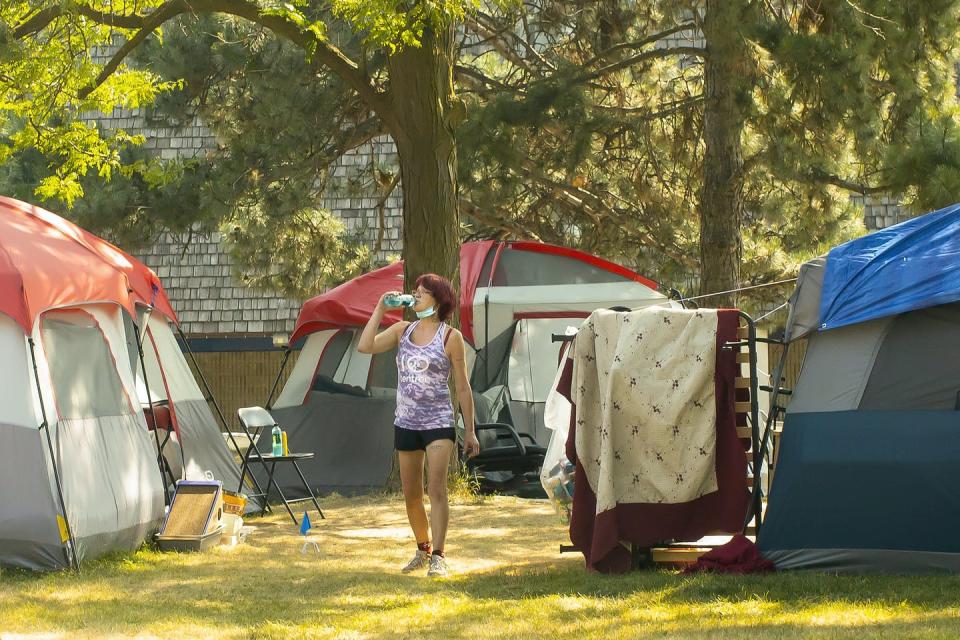 A woman drinks from a plastic water bottle as she walks through a bunch of tents at a homeless encampment