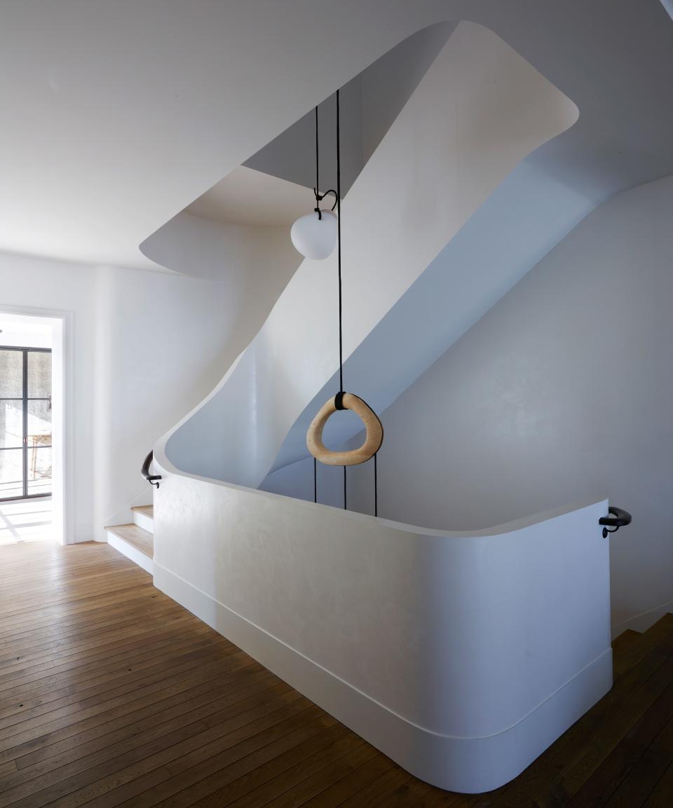 The linearity and depth of a sculptural pendant by Jérôme Pereira via Galerie Philia creates contrast in a curvaceous stairwell.