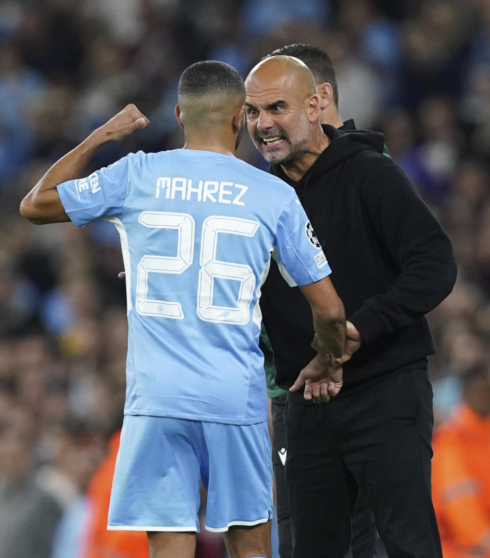 Manchester City's Riyad Mahrez speaks with manager Pep Guardiola on the touchline during the Champions League Group A soccer match between Manchester City and RB Leipzig at the Etihad Stadium, Manchester, England, Wednesday Sept. 15, 2021. (Martin Rickett/PA via AP)