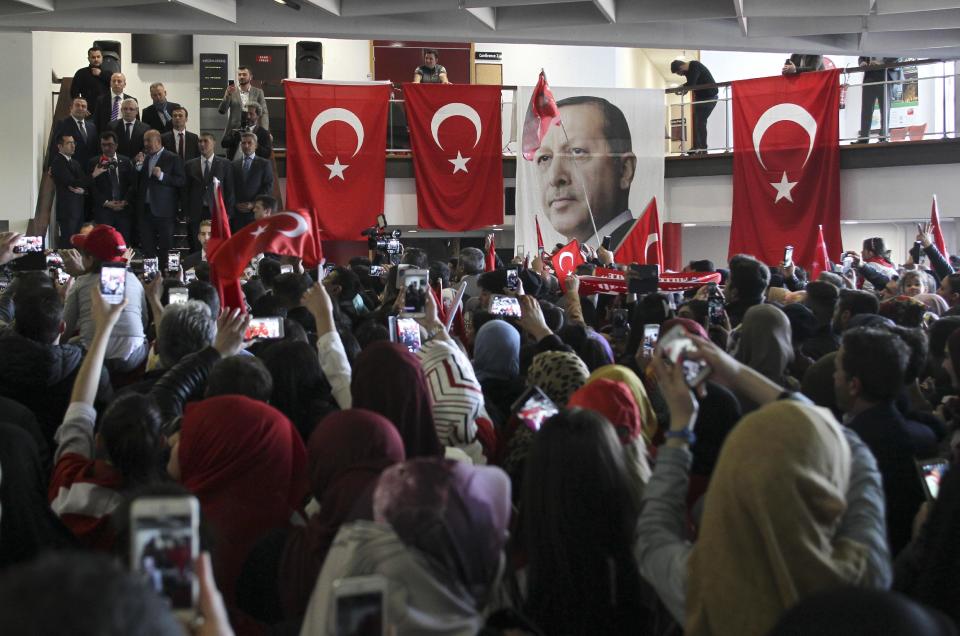 The pictures of Turkey's President Recep Tayyip Erdogan hangs on a balustrade among Turkish flags as Turkish Foreign Minister Mevlut Cavusoglu, center left, speaks during a campaign gathering in Metz, eastern France, Sunday, March 12, 2017. Foreign Minister Mevlut Cavusoglu was in France Sunday to whip up support for controversial constitutional reforms to expand the powers of the Turkish presidency. (AP Photo/Elyxandro Cegarra)