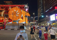 Pedestrians cross a street with a lit giant ox display to welcome the Lunar New Year at Chinatown in Singapore in Singapore Friday, Feb. 12, 2021. With Malaysian workers and students stranded in the city state over the Lunar New Year due to coronavirus travel restrictions, the Malaysian Association in Singapore has called on Malaysians to treat students to a meal. (AP Photo/Annabelle Liang)