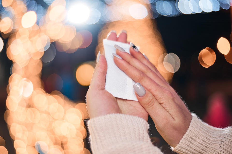 Female hands hold hand warmers on night lights background.