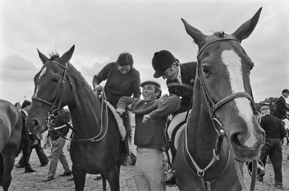 British Royal Anne, Princess Royal, dressed in riding gear as she sits on horseback, lifting her fiance, British equestrian Captain Mark Phillips, with an unspecified man, also on horseback, at the All England Jumping Course at Hickstead, an equestrian centre in West Sussex, England, July 1973. (Photo by McCarthy/Daily Express/Hulton Archive/Getty Images)