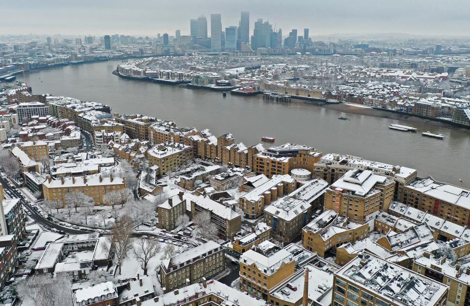 An aerial view shows a snow-covered houses and residential apartment blocks, backdropped by the River Thames and the offices and skyscrapers in the Canary Wharf business and financial district, from Wapping, east London on December 12, 2022. (Photo by Daniel LEAL / AFP) (Photo by DANIEL LEAL/AFP via Getty Images)