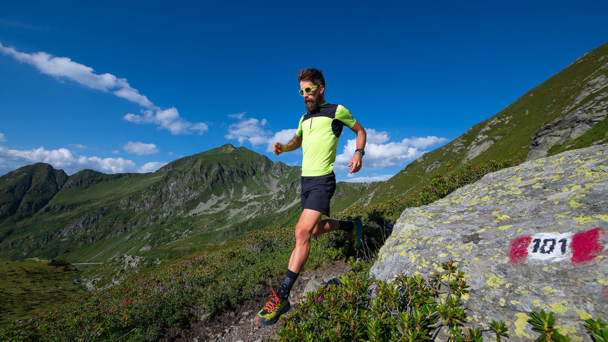  A man runs down a grassy mountainside in bright sunshine. 